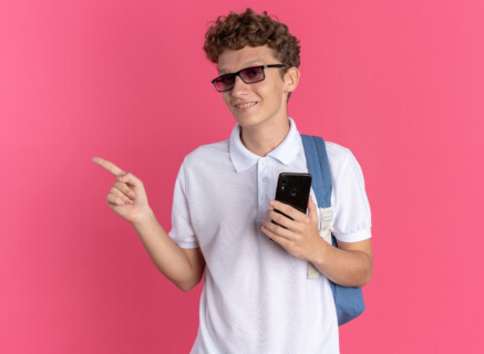 Uśmiechnięty nastolatek z plecakiem i smartfonem, symbolizujący mądre korzystanie z nowoczesnych technologii w nauce.